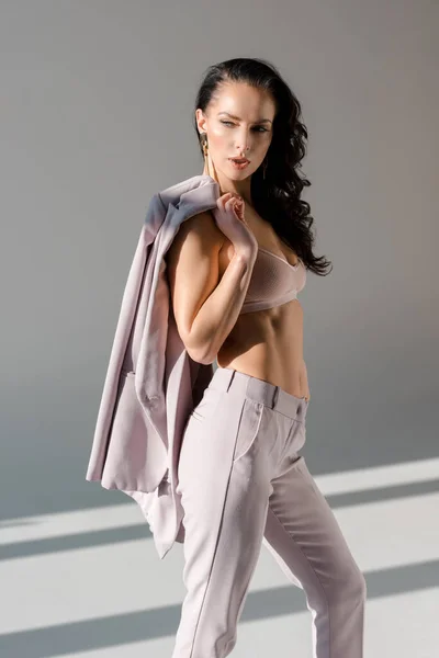 Sexy e elegante mulher no sutiã segurando jaqueta no fundo cinza — Fotografia de Stock