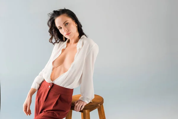 Привлекательная и сексуальная женщина в рубашке и брюках, смотрящая на камеру, изолированную на сером — стоковое фото