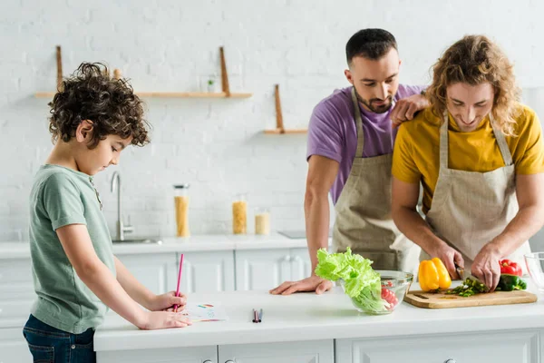 Homosexual men cooking near mixed race son drawing with color pencil — Stock Photo