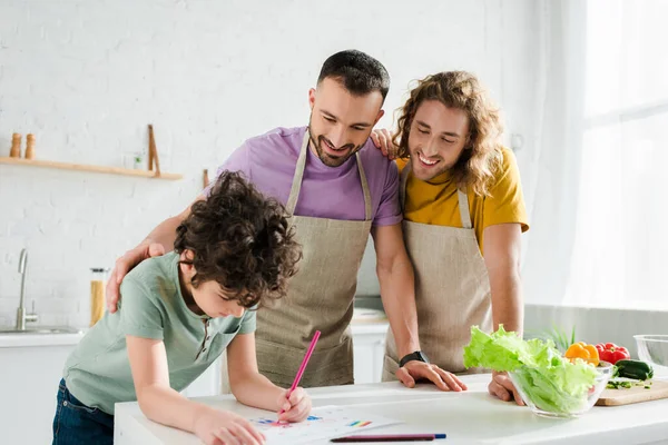 Genitori omosessuali felici guardando immagine mista disegno bambino razza — Foto stock