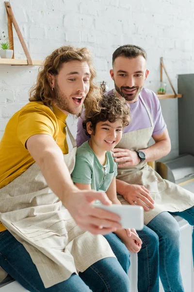 Selective focus of happy homosexual men taking selfie with mixed race son — Stock Photo