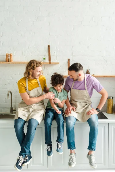 Feliz homosexual padres sonriendo cerca mixto raza hijo - foto de stock