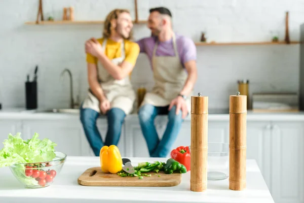 Selective focus of organic vegetables on cutting board near homosexual men in kitchen — Stock Photo