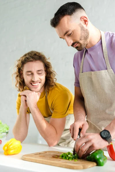 Barbudo homosexual hombre cocinar cerca pareja en casa - foto de stock
