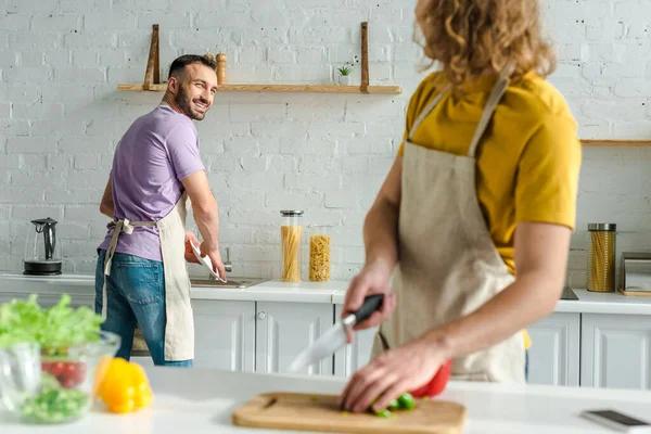 Selective focus of happy homosexual man looking at curly partner while washing plate — Stock Photo