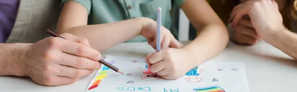 Panoramic shot of mixed race kid drawing picture with my dads lettering near homosexual parents — Stock Photo