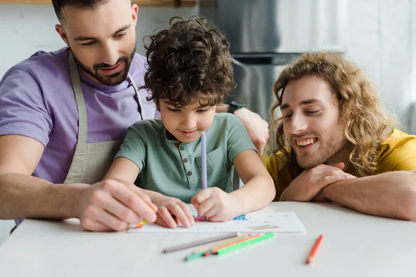 Enfoque selectivo del niño de raza mixta acercándose a padres homosexuales felices - foto de stock