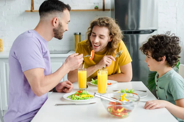 Happy homosexual men having salad with mixed race son — Stock Photo