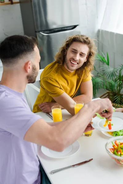 Homossexual e barbudo homem colocando salada no prato de feliz marido — Fotografia de Stock