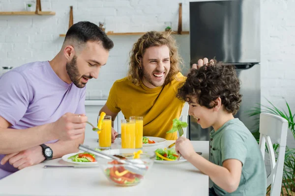 Happy homosexual men having salad with cute mixed race son — Stock Photo