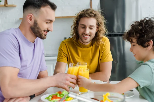 Feliz homossexual homens e misto raça filho clinking copos com suco de laranja — Fotografia de Stock