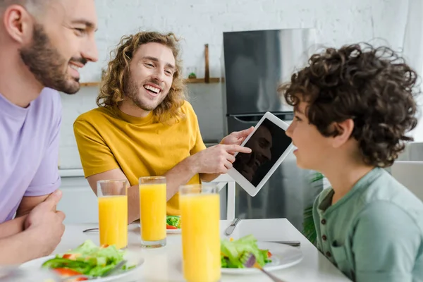 Happy homosexual man pointing with finger at digital tablet with blank screen near mixed race son — Stock Photo