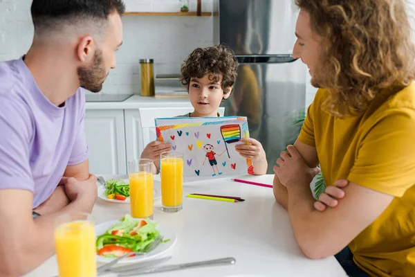 Mezclado raza niño celebración foto con lgbt bandera cerca feliz homosexual padres - foto de stock