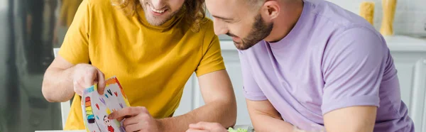 Panoramic shot of curly homosexual man pointing with finger at picture — Stock Photo