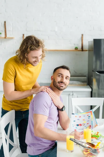 Happy homosexual men holding hands near salad and glasses with orange juice — Stock Photo