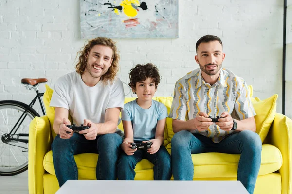 KYIV, UKRAINE - JANUARY 28, 2020: happy homosexual couple and mixed race kid playing video game — Stock Photo