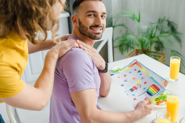 Hombres homosexuales felices tomados de la mano cerca de la imagen con la bandera lgbt - foto de stock