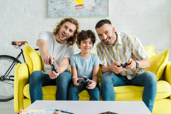 KYIV, UKRAINE - JANUARY 28, 2020: cheerful homosexual couple and mixed race kid playing video game — Stock Photo