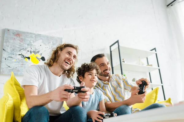 KYIV, UKRAINE - JANUARY 28, 2020: selective focus of happy homosexual couple and mixed race kid playing video game — Stock Photo