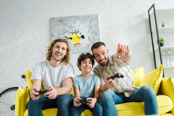 KYIV, UKRAINE - JANUARY 28, 2020: cheerful homosexual couple playing video game with mixed race son — Stock Photo