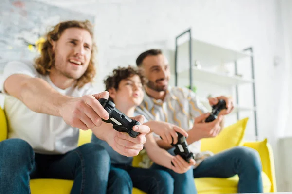 KYIV, UKRAINE - JANUARY 28, 2020: selective focus of cheerful homosexual couple playing video game with mixed race son — Stock Photo
