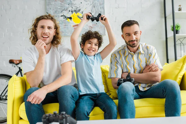 Kiew, Ukraine - 28. Januar 2020: Hübsches homosexuelles Paar spielt Videospiel mit aufgeregtem Sohn gemischter Rasse — Stockfoto