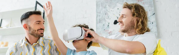 Plan panoramique de heureux parents homosexuels près de fils de race mixte en réalité virtuelle casque — Photo de stock