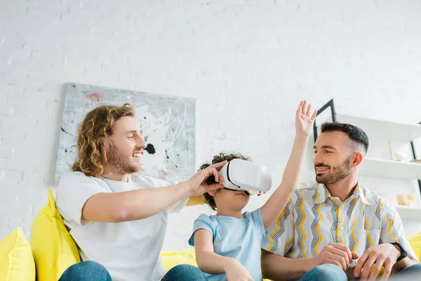 Happy homosexual parents near mixed race son in virtual reality headset — Stock Photo