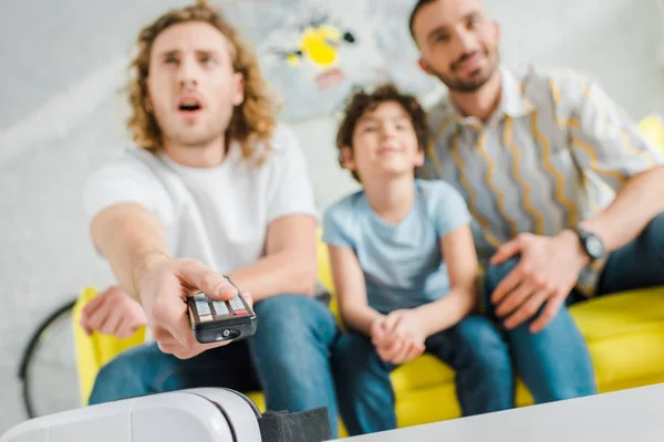 Selective focus of homosexual parents and mixed race kid watching tv — Stock Photo