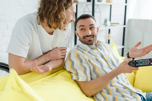 Felici uomini omosessuali sorridenti mentre guardano la tv in soggiorno — Foto stock