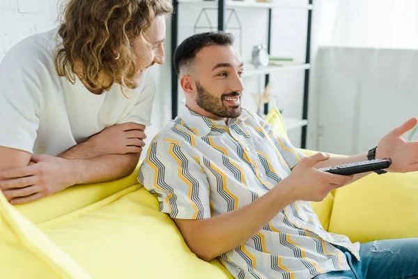 Feliz homosexual hombres sonriendo mientras viendo la película en la sala de estar - foto de stock