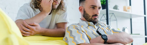 Panoramic shot of displeased homosexual men watching movie in living room — Stock Photo