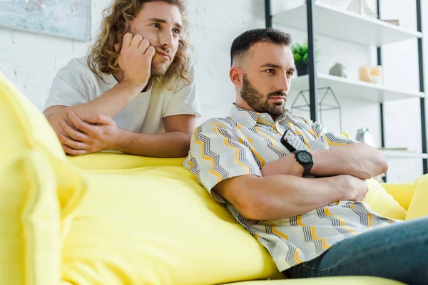 Enfoque selectivo de hombres homosexuales disgustados viendo películas en la sala de estar - foto de stock