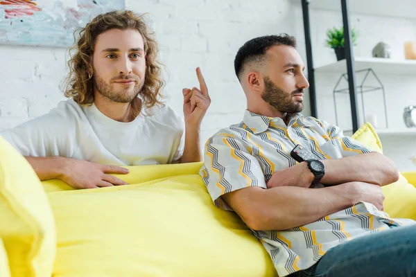 Selective focus of displeased homosexual man showing middle finger to partner while watching movie in living room — Stock Photo