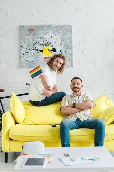 Alegre homosexual hombres sonriendo cerca lgbt bandera en casa — Stock Photo
