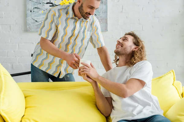 Happy homosexual men holding cup of tea at home — Stock Photo