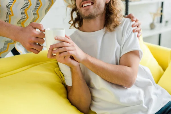 Vista recortada de hombres homosexuales felices sosteniendo la taza de té en casa - foto de stock