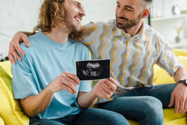 Hombres homosexuales felices sosteniendo ultrasonido escanear y mirando el uno al otro - foto de stock