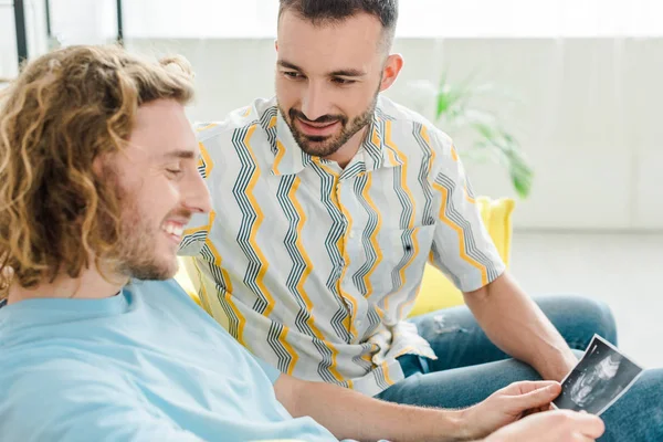 Enfoque selectivo de hombres homosexuales alegres mirando ultrasonido escaneo - foto de stock