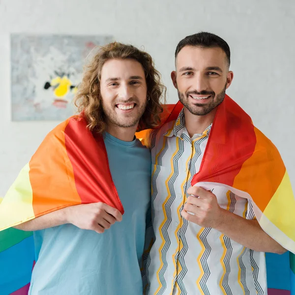 Веселі гомосексуальні чоловіки тримають прапор ЛГБТ і дивляться на камеру — стокове фото