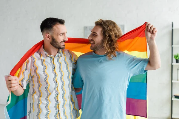 Happy homosexual men holding lgbt flag and looking at each other — Stock Photo