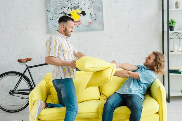 Vue latérale des hommes homosexuels heureux oreiller combats dans le salon — Photo de stock