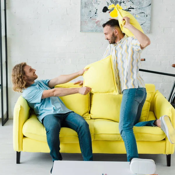 Seitenansicht von fröhlichen homosexuellen Männern Kissenschlacht im Wohnzimmer — Stockfoto