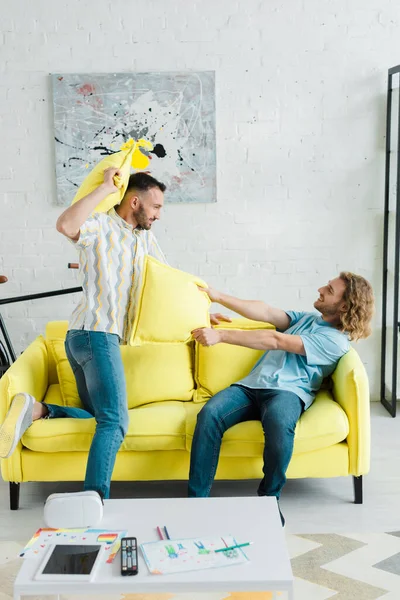 Profile of happy homosexual men pillow fighting in living room — Stock Photo