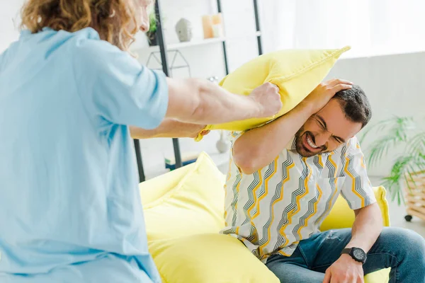 Selective focus of smiling homosexual men pillow fighting in living room — Stock Photo