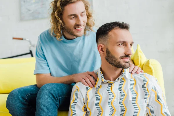 Щасливі гомосексуальні чоловіки, дивлячись далеко, сидячи у вітальні — стокове фото