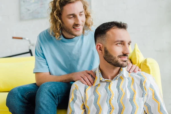 Happy homosexual men looking away while sitting in living room — Stock Photo