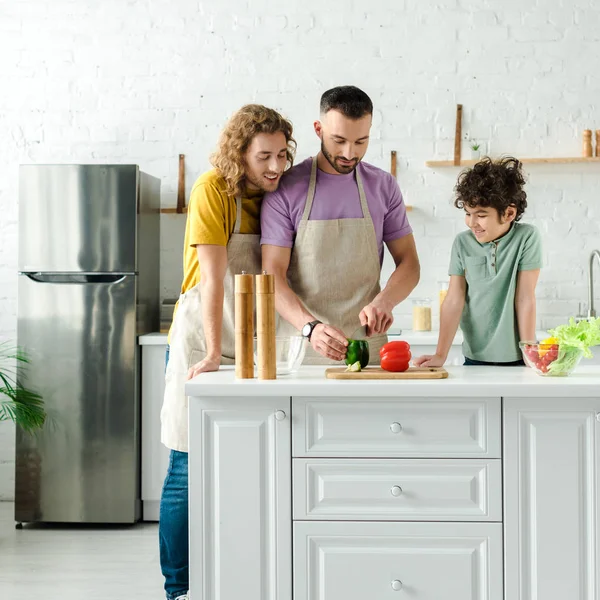 Heureux mixte race enfant près beau homosexuel parents cuisine dans la cuisine — Photo de stock