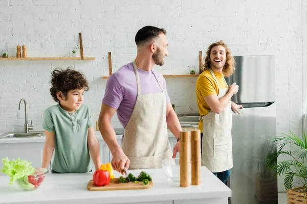 Bonito misto raça garoto perto feliz homossexual pais no cozinha — Fotografia de Stock