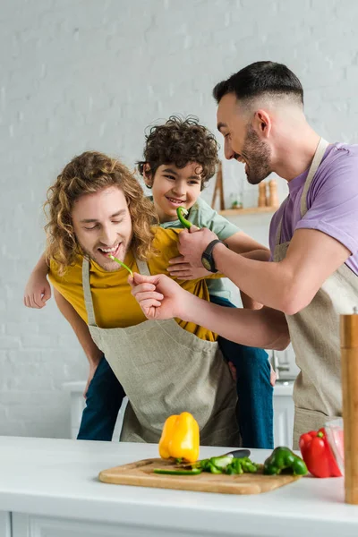 Bearded homosexual father feeding mixed race son with bell pepper near partner — Stock Photo